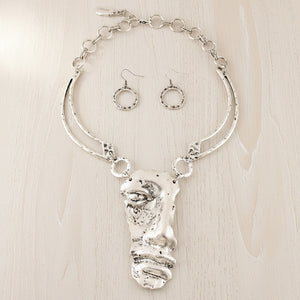 A silver-toned jewelry set featuring a textured abstract pendant necklace and matching circular drop earrings, displayed on a neutral gray background.