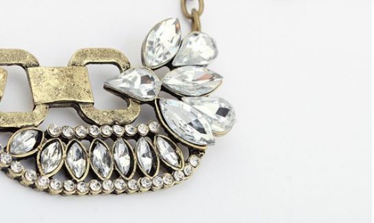 A close-up of a statement necklace featuring a textured antique gold-tone chain and a large floral cluster of clear teardrop rhinestones on a white background.