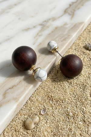 Wooden sphere earrings with marble accents on a marble and sand surface
