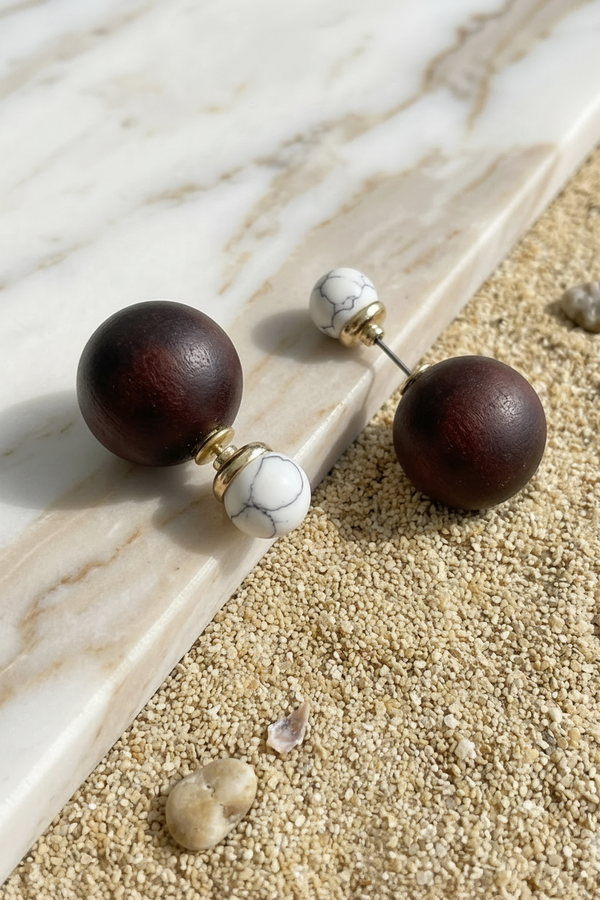 Wooden sphere earrings with marble accents on a marble and sand surface