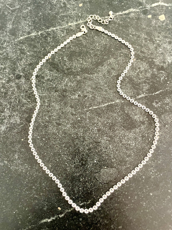 A delicate silver ball chain necklace laid flat on a dark, textured stone surface.