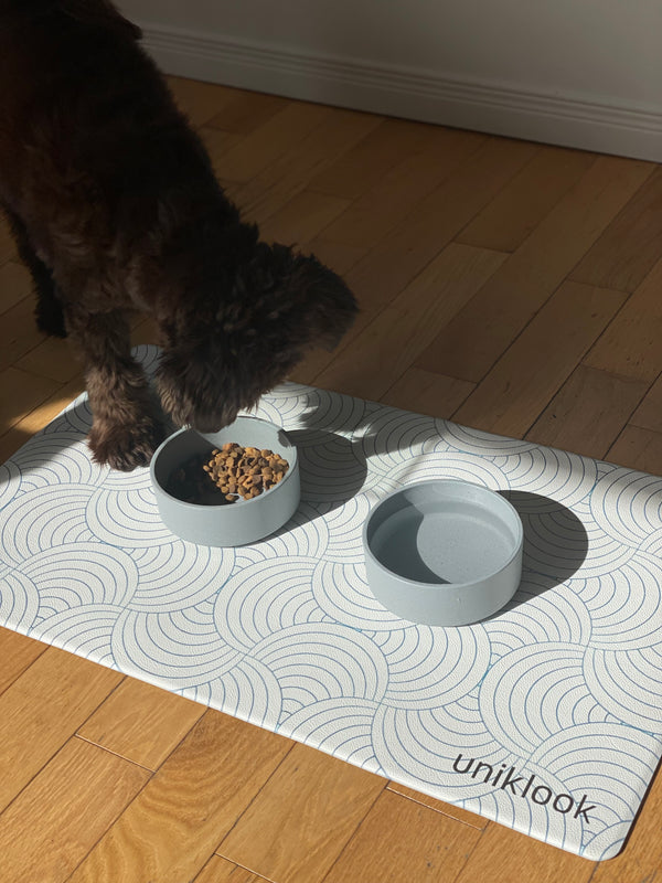 Dog eating from a bowl on a branded mat with a wooden floor background