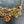 Load image into Gallery viewer, A close-up of a multi-strand statement necklace featuring antique gold-tone chains, faceted amber glass beads, and textured crystal clusters on a dark gray stone background.
