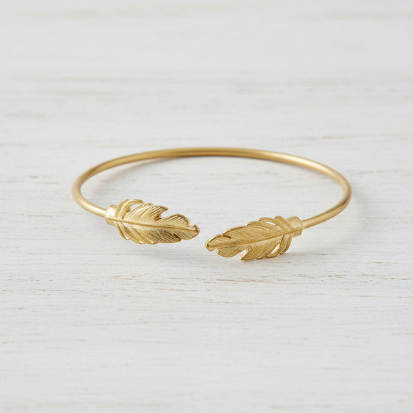 Gold bracelet with feather designs on a white background
