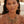 Load image into Gallery viewer, A close-up of a woman wearing a chunky gold-toned statement necklace with dangling charms and matching drop earrings, set against a softly blurred warm outdoor background.
