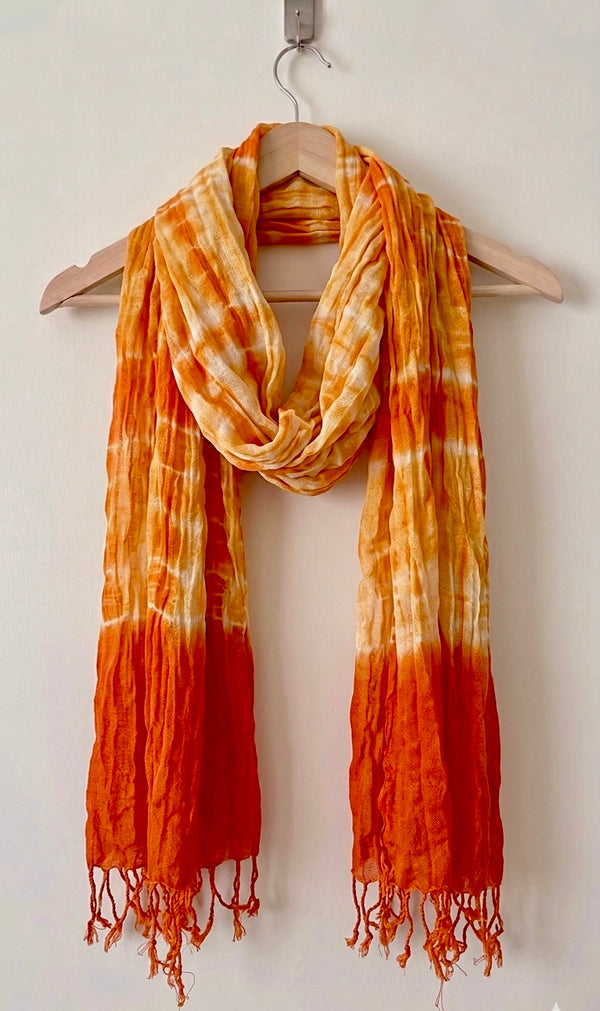 Orange and yellow tie-dye scarf on a wooden hanger against a white background
