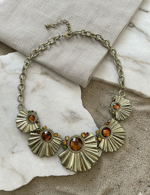 Necklace with sunburst designs and amber-colored stones on a marble surface