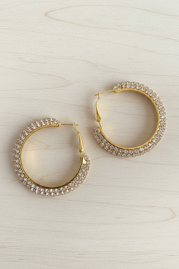 Gold hoop earrings with clear gemstones on a dark textured surface