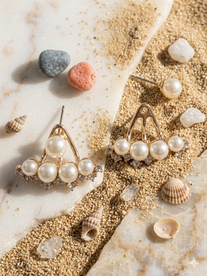 Pearl earrings on a textured surface with stones and shells