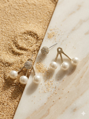 Set of pearl and gold earrings on a marble surface with sand.