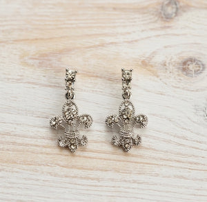 Pair of silver fleur-de-lis earrings on a light wooden surface