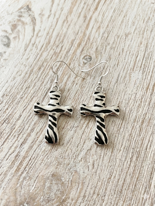 Silver cross-shaped earrings on a wooden surface