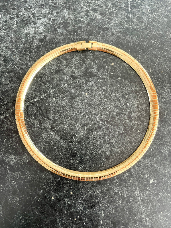 A gold-toned metal link chain necklace or choker laid flat on a dark gray textured surface.