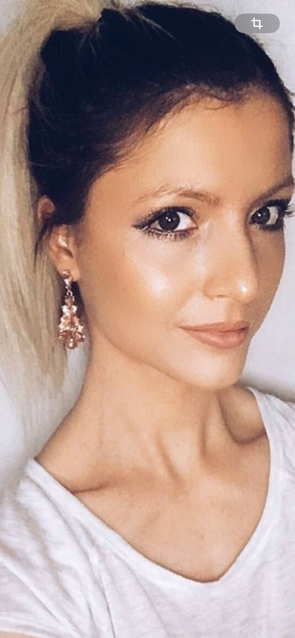 Woman with a ponytail wearing earrings and a white top against a plain background