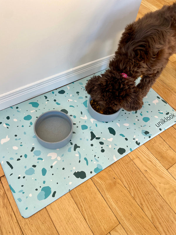 Dog drinking from a bowl on a terrazzo-patterned mat with 'unikook' branding.