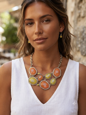 A woman wearing a chunky statement necklace with large oval orange and yellow cabochons set in silver, paired with matching drop earrings and a white sleeveless top.