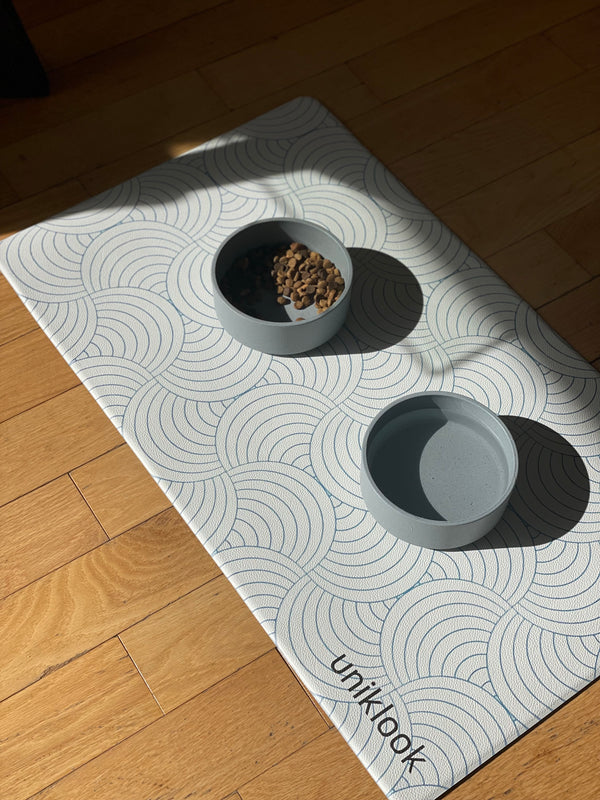 Two gray bowls on a patterned mat with 'uniklack' branding on a wooden floor.