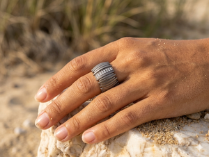 Hand wearing a silver ring on a rocky surface with a natural background