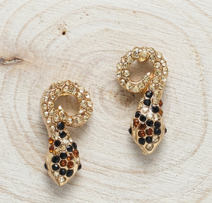 Gold and black snake-shaped earrings on a wooden surface