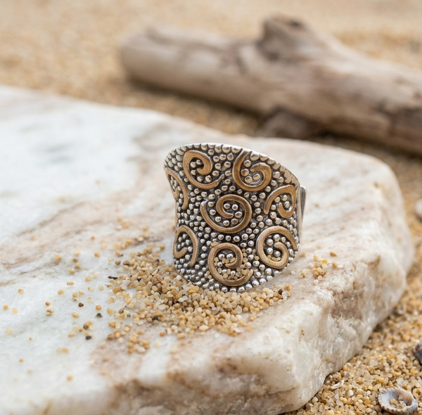 Decorative silver ring on a rock with sand and driftwood in the background