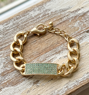 Gold chain bracelet with a green gemstone clasp on a wooden surface