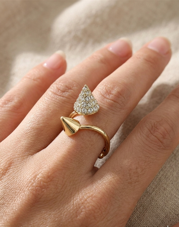Gold ring with a diamond-shaped design on a hand against a neutral background