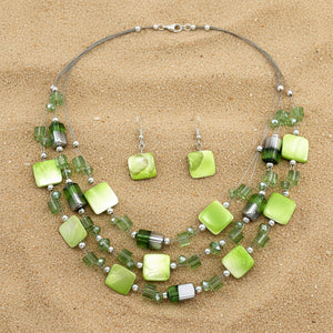 A green beaded jewelry set featuring a multi-strand statement necklace and matching drop earrings with square and cylindrical beads in various shades of green, including lime, forest, and gradient styles, accented with silver-toned beads on a white background.