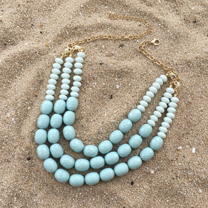 Turquoise beaded necklace with gold chain on a light pink background