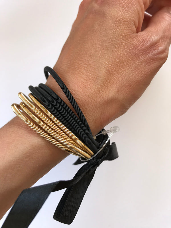 Hand wearing multiple gold and black hair ties on a white background