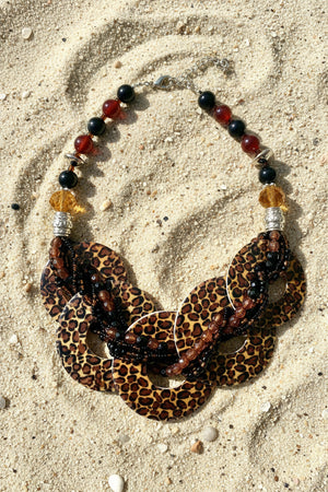 A statement necklace and matching drop earrings featuring leopard print resin discs, black beads, and red beads on a white background.