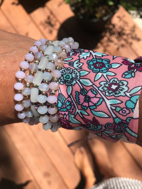 Hand wearing a beaded bracelet with a floral-patterned fabric strip on a wooden surface