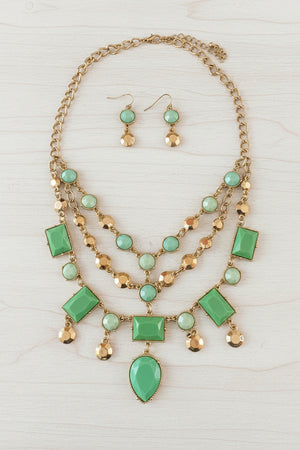 Necklace with green gemstones and gold chain on a dark surface