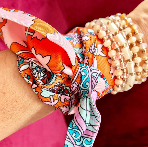 Colorful patterned headband with a pink and orange design, worn by a person with a beaded bracelet on a red background.