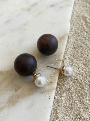 Pair of earrings with dark wooden spheres and pearl-like ends on a marble surface.