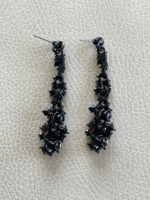 Pair of black earrings on a light gray textured surface