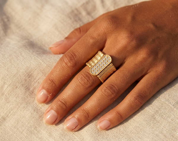 Hand wearing a gold ring with gemstones on a beige fabric background