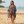 Load image into Gallery viewer, A woman walking on a sandy beach wearing a sheer, open-front patterned cover-up with tassels over denim shorts. The cover-up features a geometric design in navy blue, beige, brown, and light blue.

