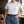 Load image into Gallery viewer, A woman wearing a plain white short-sleeve crewneck t-shirt tucked into blue jeans with a black belt featuring a large decorative silver-toned buckle, standing in a loft-style room with brick walls and windows.
