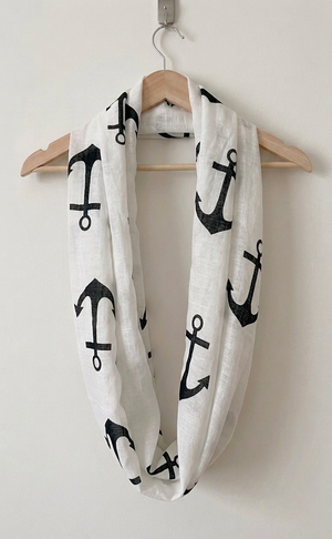 White infinity scarf with black anchor patterns draped over a wooden hanger on a white background.