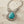 Load image into Gallery viewer, A silver filigree statement necklace featuring a large oval turquoise stone surrounded by clear rhinestones, displayed on a rustic light wood surface.

