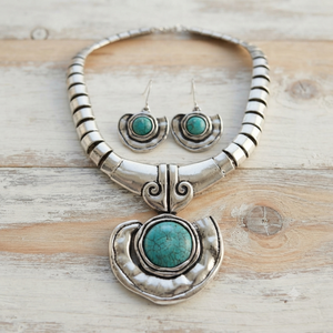 A sterling silver Southwestern-style jewelry set featuring a collar necklace and matching drop earrings, both adorned with round turquoise stones, displayed on a light wood background.