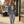 Load image into Gallery viewer, A woman walking on a city sidewalk wearing a light-wash blue denim jacket over a cream crop top, matching light-wash jeans, and white sneakers, with a brown shoulder bag.
