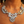 Load image into Gallery viewer, A close-up of a model wearing a statement bib necklace with large clear rhinestones and gold-tone chain links, layered over a delicate gold chain.
