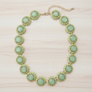 A green and gold statement necklace featuring round faceted green gemstones in textured gold bezel settings, with a gold-tone chain extender and clasp, shown on a plain white background.