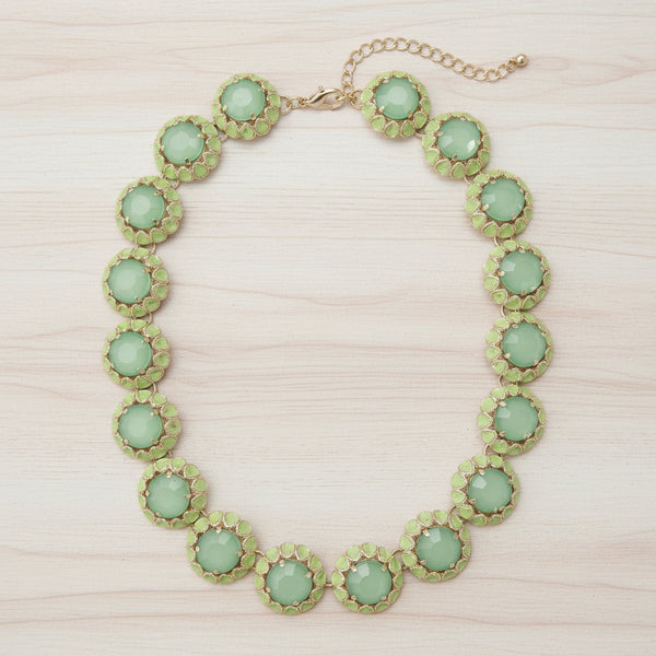 A green and gold statement necklace featuring round faceted green gemstones in textured gold bezel settings, with a gold-tone chain extender and clasp, shown on a plain white background.