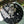 Load image into Gallery viewer, Dog sitting on a black quilted mat outdoors with plants and a fence in the background.
