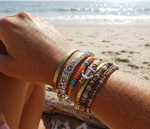 Close-up of a wrist with multiple bracelets on a beach.