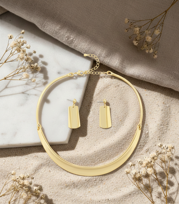 Gold necklace and earrings on a marble surface with dried flowers.