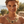 Load image into Gallery viewer, A woman wearing a chunky gold statement necklace with floral details and black centers, photographed outdoors with a blurred coastal background.
