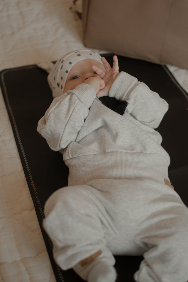 Baby in a light gray outfit lying on a black surface with a neutral background